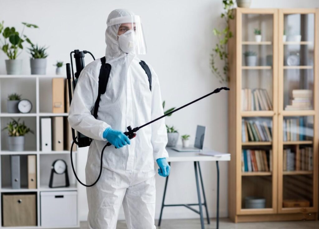 Pest control technician in protective gear spraying for cockroach elimination.